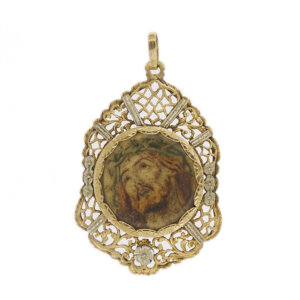 Ciondolo antico in oro giallo e oro bianco 18 kt con raffigurazione del viso di Cristo in croce, contorno traforato con decorazioni diamantate e fiorellini, retro con fiore e foglie incise.