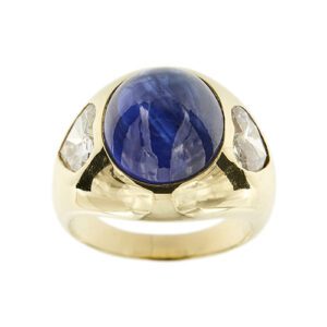 Anello a fascia bombata in oro giallo 18kt con zaffiro ovale cabochon da 12 ct e ai lati 2 diamanti a cuore da 0.95 ct e 0.75 ct - colore FG e purezza VS; Pederzani è una boutique storica di lusso di Milano.