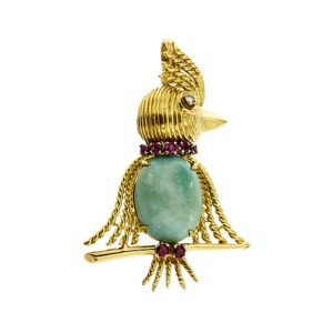 Ciondolo a forma di pappagallo sul trespolo con ali e creta a fili attorcigliati in oro giallo 18kt, testa a righe e come occhio un diamante taglio huit huit da 0.03 ct, corpo con turchese ovale taglio cabochon e al collo e sulle zampe 7 rubini da 0.05 ct cad.