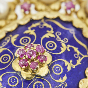 zoom dettaglio rubini a forma di fiore e smalto blu al centro di spilla ciondolo in oro giallo