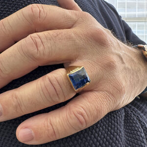 Foto gioiello indossata: anello in oro giallo a scudo chevalier con pietra blu zaffiro quadrato