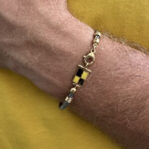 Foto gioiello indossata: bracciale in acciaio uomo semi rigido con inserti in oro giallo e bandierina nautica gialla e blu smaltata