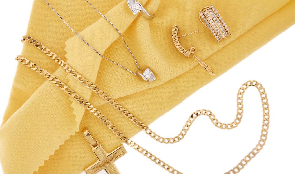 Foto banner home 1: come pulire i gioielli in oro? In foto: gioielli in oro su sfondo giallo: ciondolo croce, collana maglia grumette, collana punto luce con diamante in oro bianco, anello solitario con diamante in oro bianco e orecchini a lobo con diamanti.