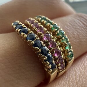 Foto gioiello indossata: anello tripla riviere in oro giallo ad onda con rubini, smeraldi e zaffiri